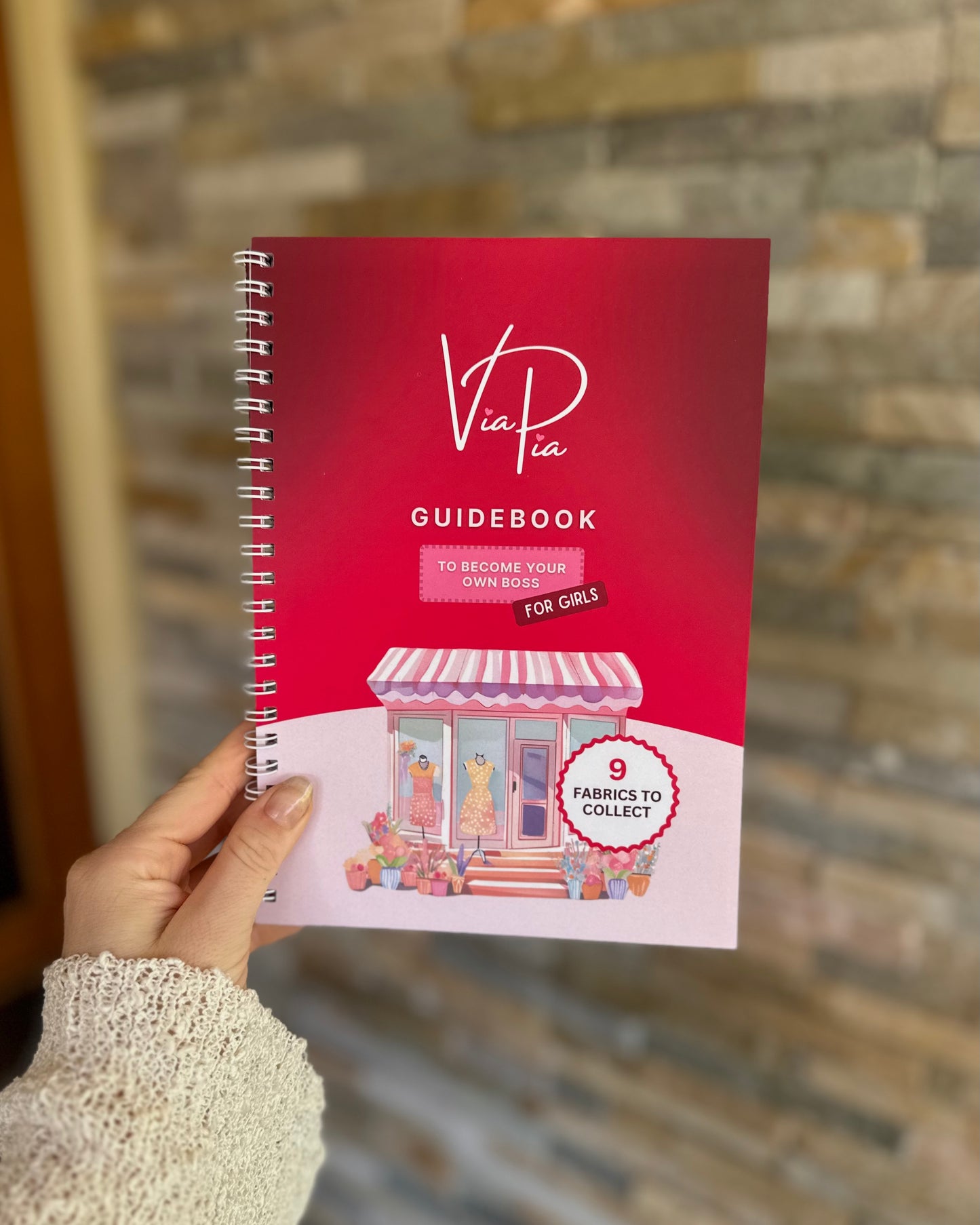 Front cover of the Via Pia Junior Business Guidebook held in hand, introducing kids to business through creativity and crafting.