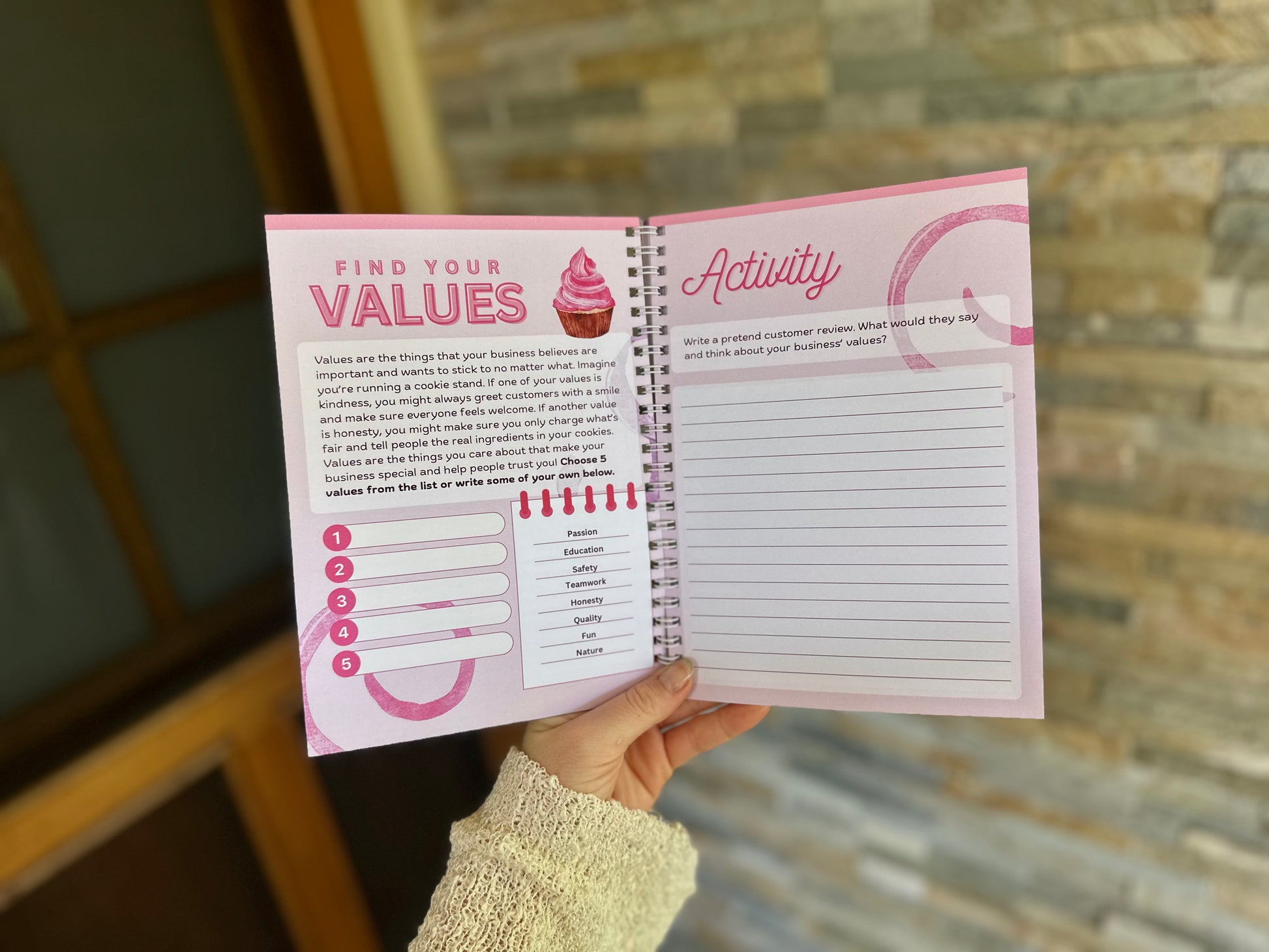 Branding section of the Via Pia Junior Business Guidebook, open to the values activity pages, held in hand.