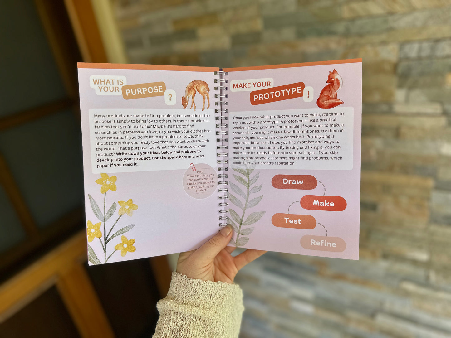Product section of the Via Pia Junior Business Guidebook, open to purpose and prototype activity pages, held in hand.
