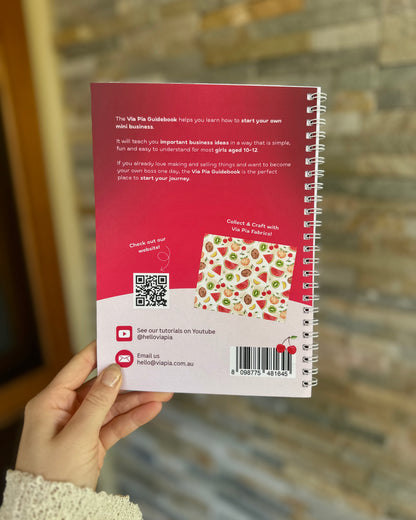Back cover of the Via Pia Junior Business Guidebook held in hand, showing an overview of what girls learn inside.