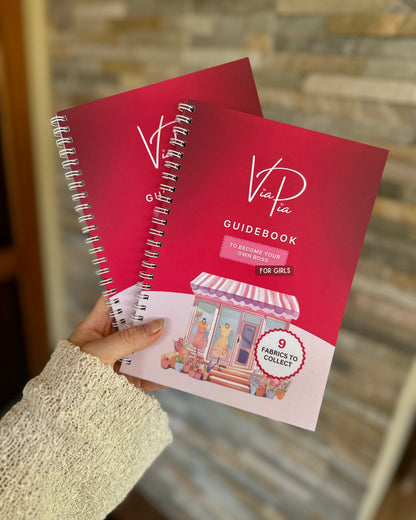 Via Pia Junior Business Guidebook for girls, two copies stacked and held in hand showing the front cover.