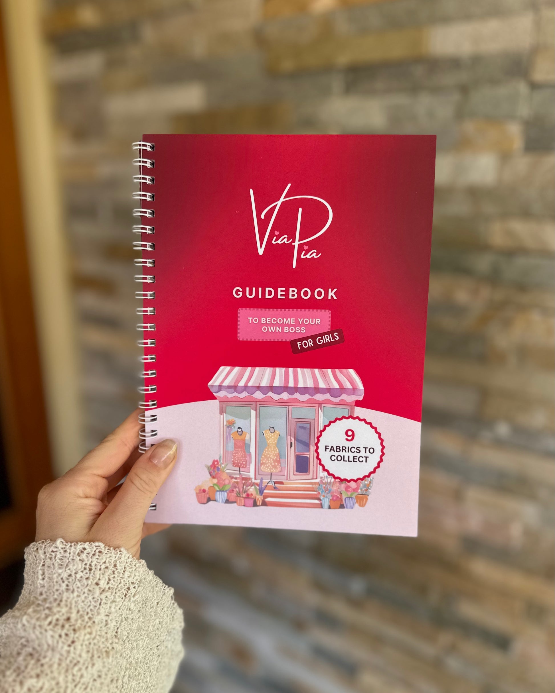 Front cover of the Via Pia Junior Business Guidebook held in hand, introducing kids to business through creativity and crafting.